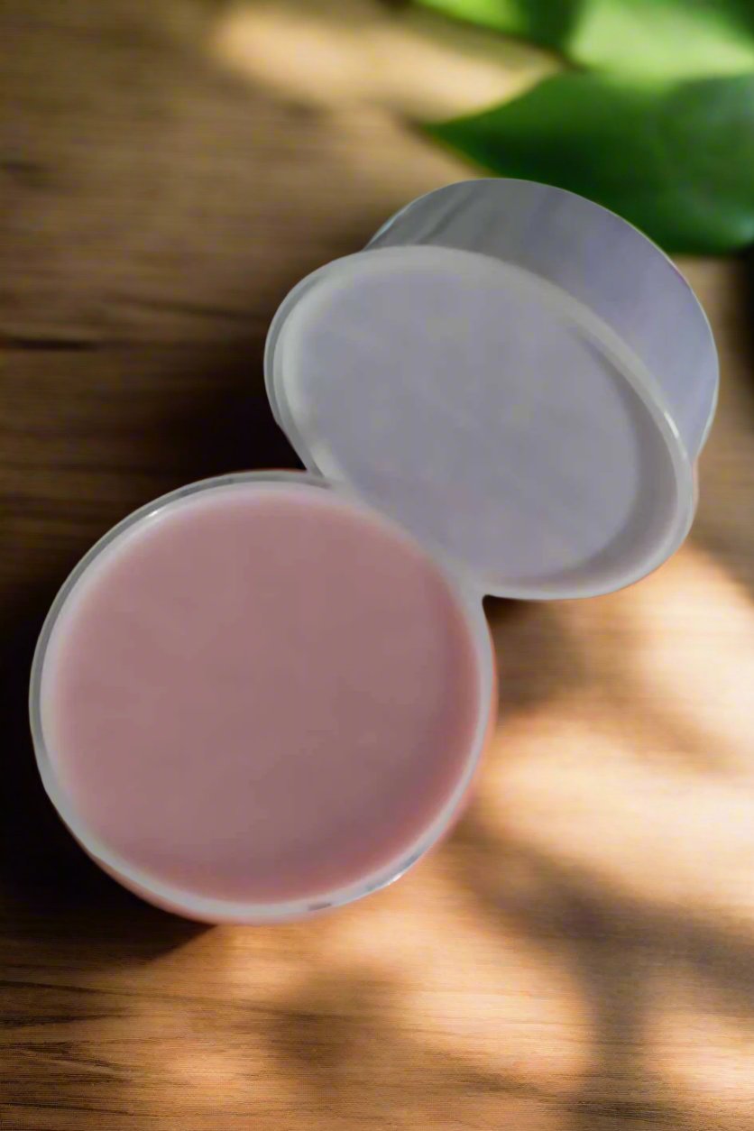 Open container of pink all-natural wax melts on wooden surface with green leaves in the background.