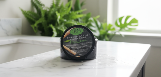 Black salt scrub container on a marble surface with plants in the background